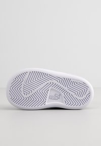 Semelle d'une chaussure Puma blanche montrant un motif de bande de roulement en zigzag et le texte "non-marking" sur un fond gris clair.