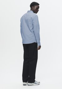 Light blue button-up shirt made of cotton, paired with black trousers and predominantly white sneakers with blue accents.