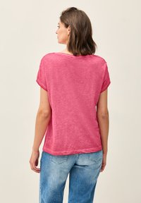 Pink, short-sleeved top with a relaxed fit, made of a soft, lightweight fabric. Round neckline and subtle stitching details. Paired with light blue jeans.