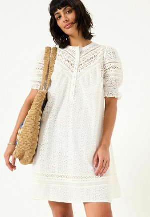 Weißes Spitzenkleid mit kurzen Puffärmeln, Knopfverschluss und kunstvollen Spitzenverzierungen am Ausschnitt und Saum. Leichter Stoff.