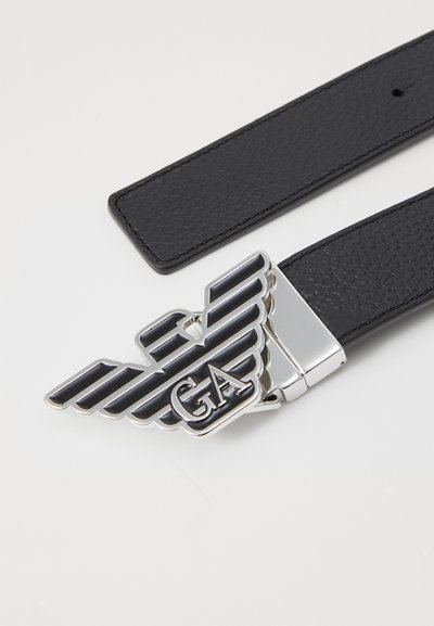 Must must leather vöö, millel on suur hõbedane tiibadega lõpp, musta ja valge triibuga ning "GA" logo. Sujuv tekstuur ja teravad otsad.