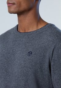 Szary sweter wykonany z miękkiego materiału, z okrągłym dekoltem i małym logo w ciemnym niebieskim na piersi.