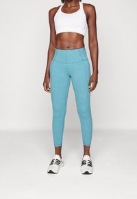 Niebieskie legginsy sportowe wykonane z teksturowanej tkaniny, zestawione z białym stanikiem sportowym i czarno-białymi butami sportowymi.