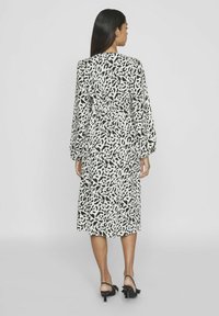 Dolga obleka midi z dolgimi rokavi v črno-beli abstraktni vzorčni zasnovi, izdelana iz gladkega blaga, s poudarjeno pasom in raztegnjenim krilom.