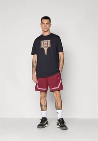 Tumesinine T-särk korvpallivõrgu graafikuga, kombineeritud burgundia pükstega, millel on valged aktsendid, kantud mustade ja roheliste spordijalatsitega.