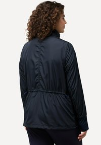Granatowa kurtka przeciwwiatrowa z wąskim pasem, gładką teksturą, wysokim kołnierzem i długimi rękawami z elastycznymi mankietami. Tylny widok ukazuje szczegóły projektu.