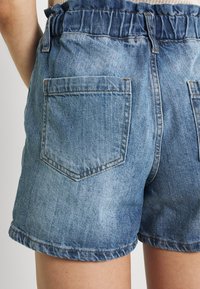 Shorts de mezclilla con un lavado azul claro, cintura elástica con volantes y dos bolsillos traseros. Textura desgastada con costuras visibles.