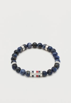 Perlenarmband mit dunkelblauen und schwarzen Steinen, silbernen zylindrischen Abstandshaltern und einem silbernen Verschluss, der mit rot-weiß-blauen Streifen graviert ist.