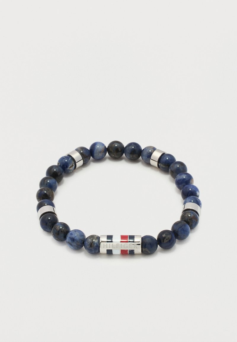 Bracelet à perles avec des pierres bleu foncé et noires, des entretoises cylindriques en argent, et un fermoir en argent gravé de rayures rouges, blanches et bleues.