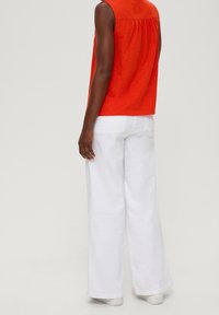 Červený rukávový top bez rukávů se staženým zadním dílem v kombinaci s volnými bílými kalhotami. Oblečení má ležérní střih a je vyrobeno z lehkého materiálu.