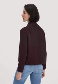 Burgunderfarbener Strickpullover mit hohem Kragen, geripptem Muster, verkürztem Design und langen Ärmeln, kombiniert mit hellblauen Jeans.