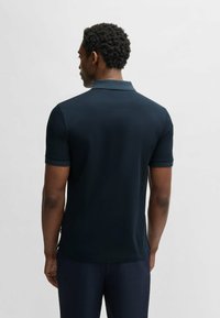 Marinblå polo med en slät tygkvalitet. Har en standardkrage, korta ärmar och en rak nertill. Enkelt och funktionellt design.