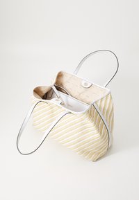 Sac en toile rayé jaune et blanc avec des poignées blanches lisses, un intérieur beige présentant un motif de logo subtil et un détail de fermeture à pression.