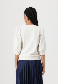 Helles Cremefarbene Sweatshirt mit gepufften Ärmeln und geripptem Saum. Kombiniert mit einem tiefblauen, plissierten Rock. Geschmeidige Textur, lässiges Design.