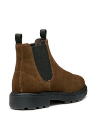 Botas Chelsea de ante marrón con paneles elásticos en los laterales, con una suela de goma negra y dos lengüetas para ponérselas con facilidad.