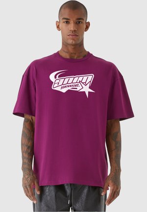 Lilla bomulds oversized t-shirt med korte ærmer og et hvidt grafisk logo på forsiden. Glat tekstur og afslappet pasform.