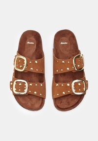Brown suede slide sandals with two straps featuring gold buckles and stud accents. Soft interior with a textured surface.