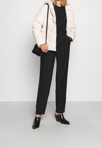 Ljusrosa puffjacka med huva, kombinerad med en svart tröja och höga svarta byxor. Svarta klackskor fulländar looken.