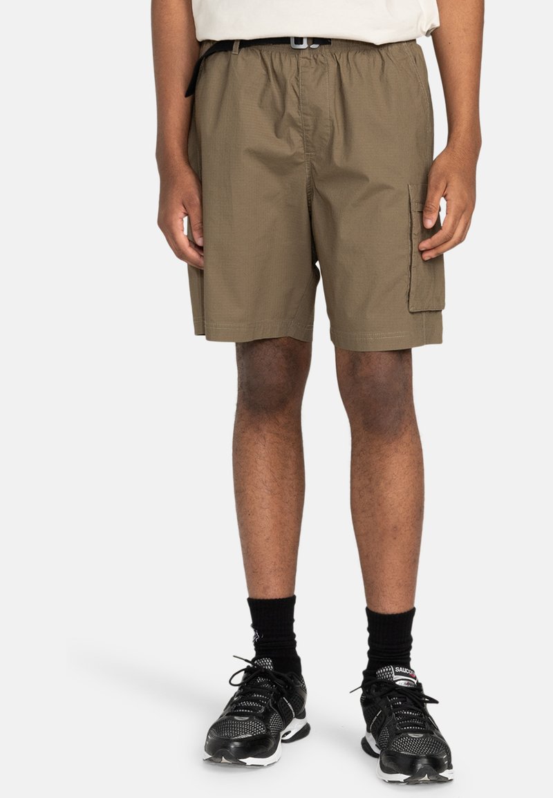 Khaki Cargo-Shorts mit elastischem Bund, Seitentaschen und leichtem Stoff. Kombiniert mit schwarzen Sportschuhen und Socken.