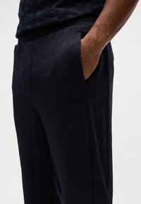 Pantaloni navy in tessuto strutturato con un motivo geometrico. Presenti tasche laterali e un logo discreto sulla coscia sinistra.