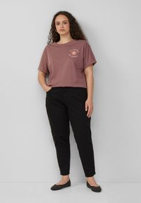 Overmaatse mauve t-shirt met opgerolde mouwen, voorzien van een zonafbeelding en tekst. Gepaard met zwarte slim-fit broeken en zwarte studschoenen.