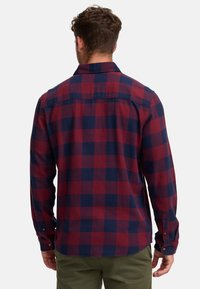Camisa de franela a cuadros en rojo y azul marino, con mangas largas, puños con botón y un dobladillo redondeado. Textura suave con un patrón de cuadros clásico.