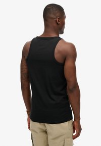 Czarny bawełniany top na ramiączkach o klasycznym kroju, z prążkowanym dekoltem i bez rękawów. Gładka faktura, bez widocznych wzorów czy akcentów.