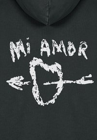 Felpa nera con cappuccio caratterizzata da testo bianco che recita "Mi Amor", accompagnato da una forma a cuore con una freccia che la attraversa. Materiale in cotone con una texture liscia.