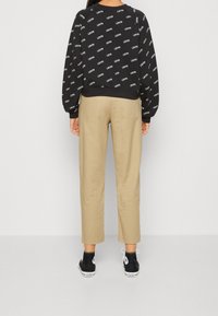 Felpa nera con motivo di logo ripetuto, abbinata a pantaloni beige. Sneakers nere con suole bianche e dettaglio del logo.