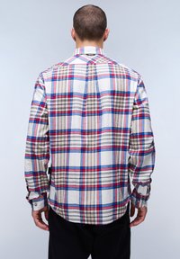 Camisa de franela a cuadros en blanco, rojo, azul y beige; de manga larga, con cuello y puños abotonados; presenta un dobladillo curvado y una etiqueta colgante.