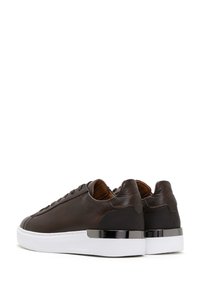 Baskets en cuir marron foncé avec semelles blanches épaisses et accents métalliques noirs au niveau du talon, présentées de dos et de profil.