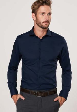 Navy blue button-up shirt with a spread collar, long sleeves, and a smooth texture. Worn with a brown belt and gray trousers.