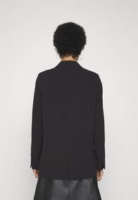 Blazer noir avec une coupe ajustée, col cranté, manches longues et texture lisse. Vue de dos, avec des poignets boutonnés et un design simple.