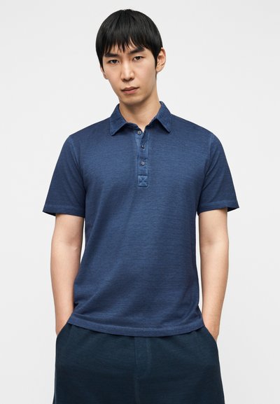 Πουκάμισο πόλο με κοντά μανίκια σε σκούρο μπλε ύφασμα, με γιακά, πατιλέτα με τέσσερα κουμπιά και διακριτικό υφασμάτινο μοτίβο.