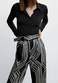 Black long-sleeve button-up shirt paired with high-waisted black and white striped wide-leg pants featuring a belt and bold geometric pattern.