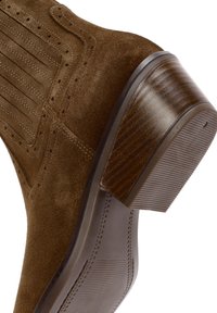 Brown suede boot with elastic side panel and stitched detailing, featuring a stacked wooden block heel and rubber sole grip.