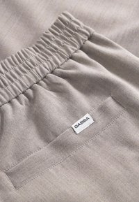 Helles graues Gewebe mit einem gerafften, elastischen Bund und einer Tasche, die ein kleines Etikett mit der Aufschrift "GABBA" trägt. Weiche Textur und glatte Oberfläche.