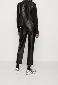 Schwarzes Kunstlederoberteil mit einem eleganten Design, kombiniert mit schwarzen Kunstlederhosen. Das Outfit wird durch sportliche weiße Sneakers ergänzt.