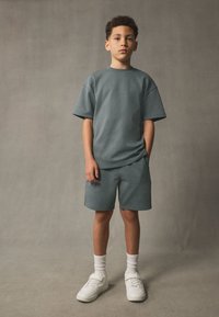 Graues T-Shirt- und Shorts-Set aus Baumwollmischung mit lockerem Schnitt, kombiniert mit weißen Sneakers und gerippten weißen Socken.