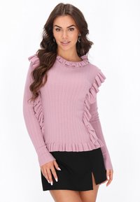 Jersey de manga larga con canalé en rosa claro, con detalles de volantes en el escote y en el costado, combinado con una mini falda negra.