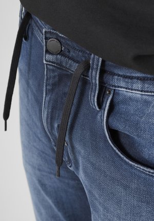 Jeans in denim blu scuro, con coulisse nera e chiusura con bottone, dotati di tasche visibili e una superficie in tessuto strutturato.