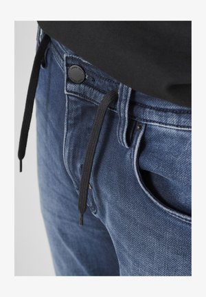 Jeans in denim blu scuro, con coulisse nera e chiusura con bottone, dotati di tasche visibili e una superficie in tessuto strutturato.