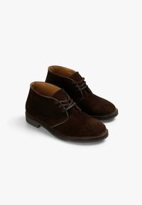 Botas de ante marrón hasta el tobillo con puntera redonda, diseño de cordones y suela de goma plana. El interior cuenta con un forro liso en tono marrón.