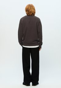 Dark gray sweatshirt with a relaxed fit, ribbed cuffs, and hem, worn over a white shirt. Paired with loose black trousers and black footwear.