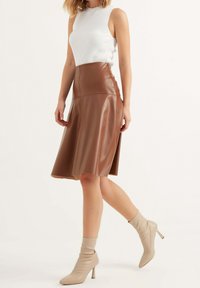 Gonna midi in finta pelle marrone con silhouette svasata, abbinata a un top senza maniche bianco a coste e stivali beige alla caviglia.