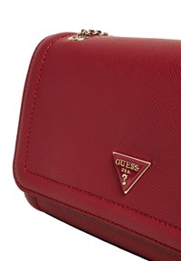 Sac à main synthétique rouge avec surface texturée, quincaillerie dorée et accent logo triangulaire. Il dispose d'une fermeture zippée et d'une couture détaillée.