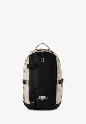 Zaino piccolo nero e beige con fascia frontale, fibbie laterali, manico superiore e logo "TIGHT SMALL" sul pannello frontale.