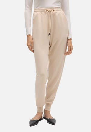 Pantalones jogger beige con cordón, combinados con una blusa blanca de manga larga y bailarinas negras de punta con tiras finas.