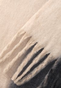 Bufanda de lana con un degradado que va de crema a gris oscuro, con bordes deshilachados. Textura suave, ligera y diseño con capas suaves.