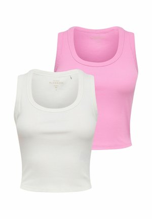 Kvinde smilende iført hvid ærmeløs top, mørke vidde jeans med sort nittebælte, der holder en sort håndtaske, mens hun går.